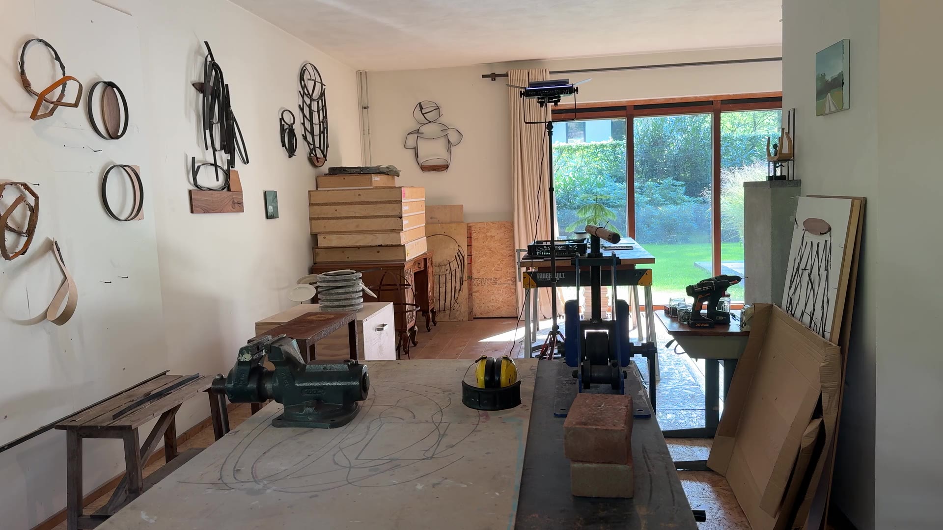 Het atelier van Ine Boeijen: metalen wandobjecten, werktafels en een raam naar de tuin